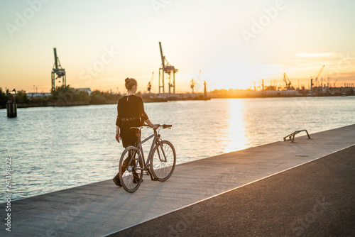 Young woman with her bicycle in harbour while sunset