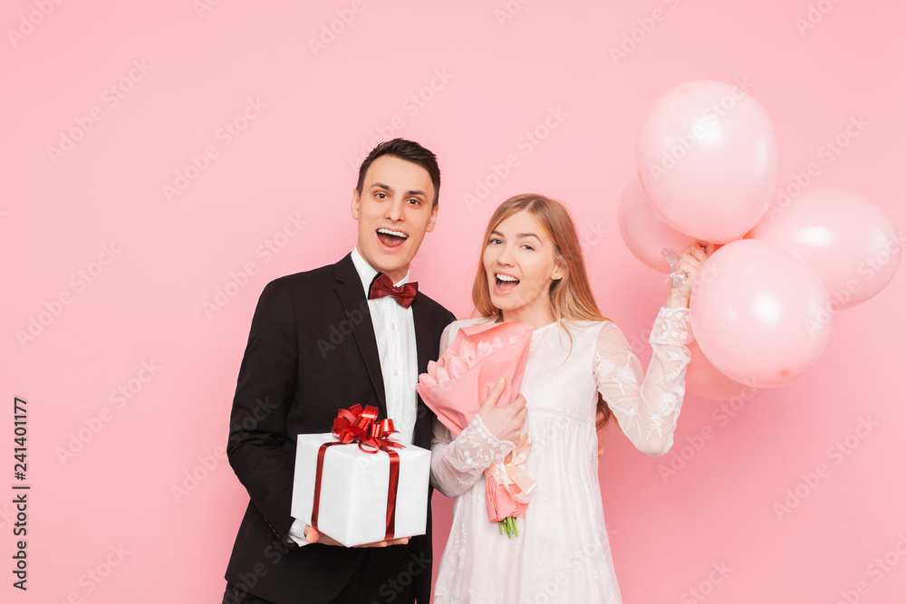 A man and a woman give each other gifts, hold gift boxes and balloons, Valentine's concept, in the studio on a pink background A man and a woman give each other gifts, hold gift boxes and balloons, Valentine's concept, in the studio on a pink background