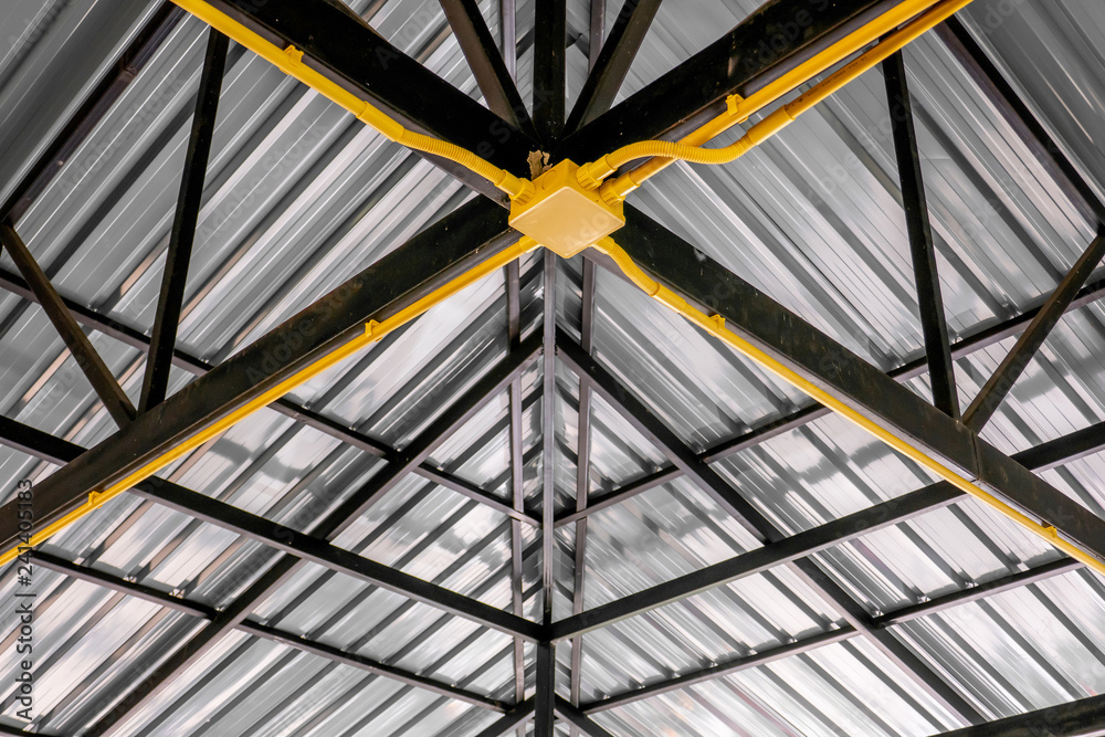 The yellow electric wire pipe on the ceiling in the house with the metal roof.