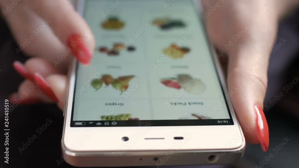 Young woman with manicure orders food home in an online store using a smartphone. Female selects the tropic fruit  in the grocery online store. Close up. 4K UHD. LOS ANGELES - October 2018.