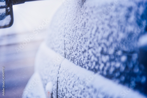 Rear view mirror on a snow-covered car, standing in the Parking lot near the house on a cold morning, the sun shines into the camera. Closeup of car tires in winter on the road covered with snow.