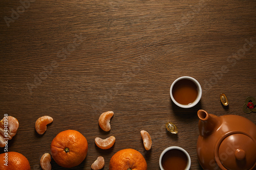 top view of tea set, tangerines and coins on wooden surface