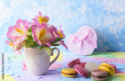 Colorful macaroons in a gift box and marshmallow in coffee cup on wooden table. Sweet macarons and flowers. 
