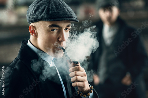 stylish men smoking in retro clothes posing on background of railway. england in 1920s theme. fashionable look of brutal confident man. atmospheric moments with smoke photo