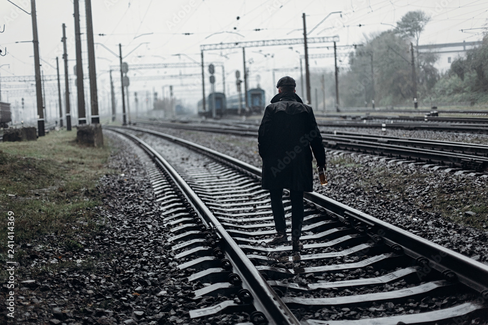 Φωτογραφία silhouette of stylish man in retro look walking in rain on background of foggy railway