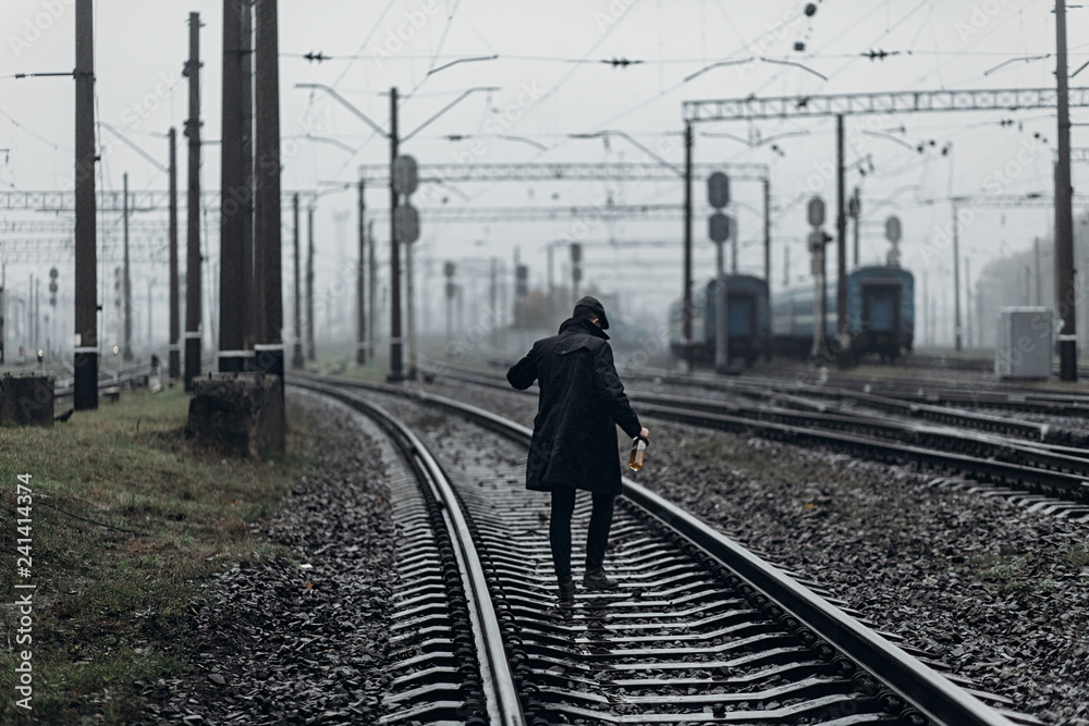 Φωτογραφία silhouette of stylish man in retro look walking in rain on background of foggy railway