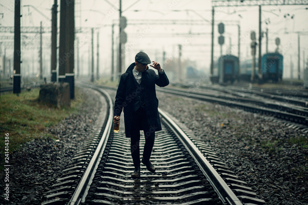 Αυτοκόλλητο silhouette of stylish gangster man with bottle whiskey walking on railway road