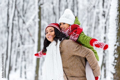 attractive african american woman giving piggyback ride to smiling daughter in winter park photo