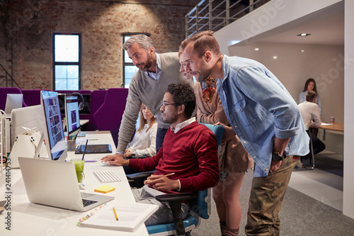 Colleagues looking over shoulder of young man working in modern office photo