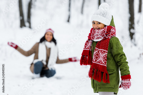cute child looking at camera and african american mother at background in winter park