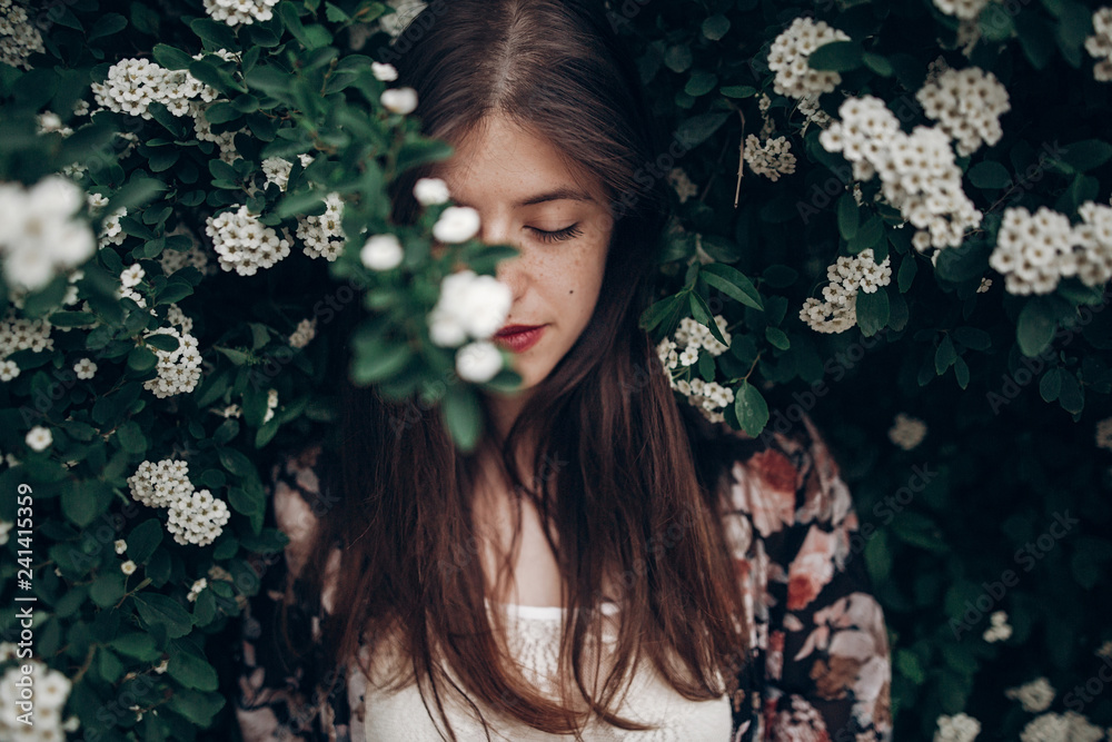 calm portrait of beautiful hipster woman in blooming bush with white flowers of spirea. boho girl sensual portrait in floral modern clothes in greenery. space for text - obrazy, fototapety, plakaty 