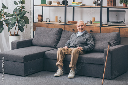senior man with grey hair sitting on sofa in living room