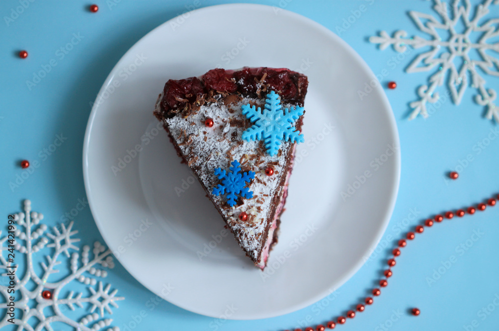Chocolate cake slice with snowflakes decoration and cherry on winter background top view.