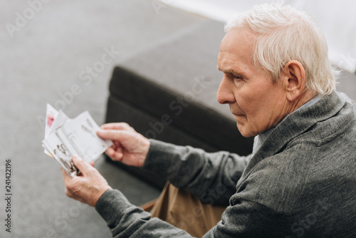 sad retired man with grey hair looking at old photos at home