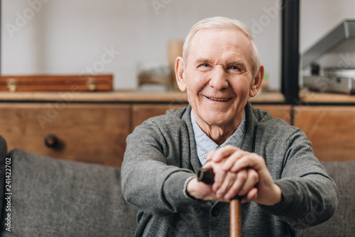 cheerful pensioner smiling and holding walking cane at home photo