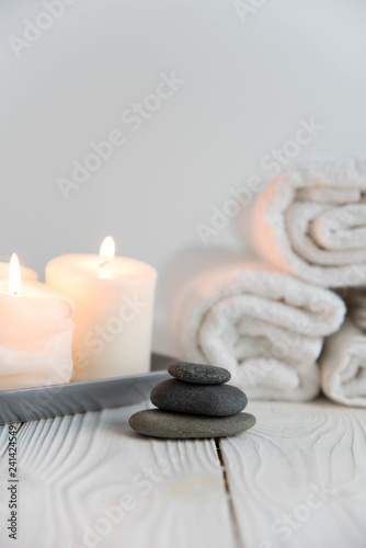 Beautiful spa still life. Twisted towel, aromatic candles and black hot stone on wooden background. Hot stone therapy. Concept of harmony, balance and meditation, relax, massage, beauty spa treatment.