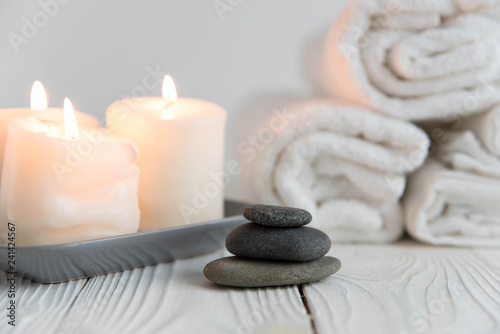 Beautiful spa still life. Twisted towel  aromatic candles and black hot stone on wooden background. Hot stone therapy. Concept of harmony  balance and meditation  relax  massage  beauty spa treatment.