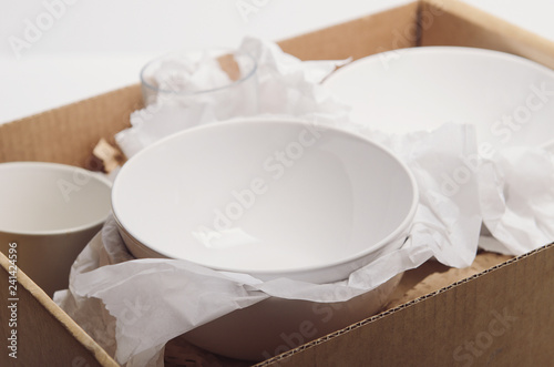 Clean white dishes in paper packed in a cardboard box. Concept relocation