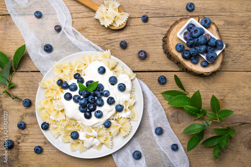 Tasty pasta with fresh organic blueberries and vanilla cream. Sweet dinner on retro wooden table.