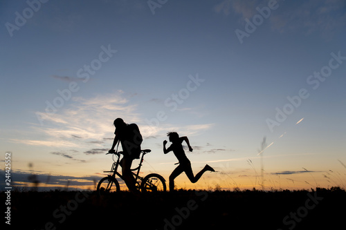people riding bike and running in meadow with sunset background