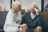 retired woman sitting near senior husband with headache