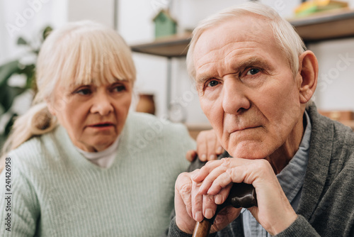 selective focus of sad pensioner sitting near retired wife at home