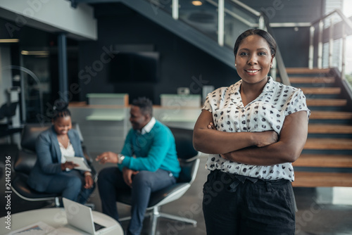 Portrait of a confident black businesswoman smiling with her arms crossed and all african team in the background
