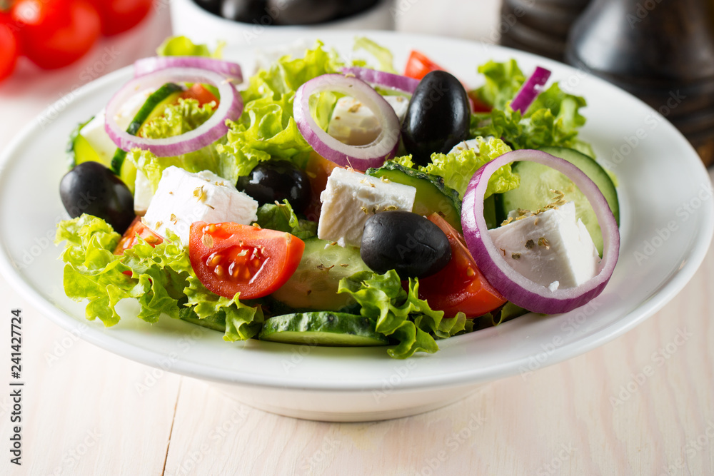 Fresh Greek salad with delicious  ruccola, spinach, cabbage, arugula, feta cheese, red onion and cherry tomato on wooden background. Oil, salt and pepper. Healthy and diet food concept.
