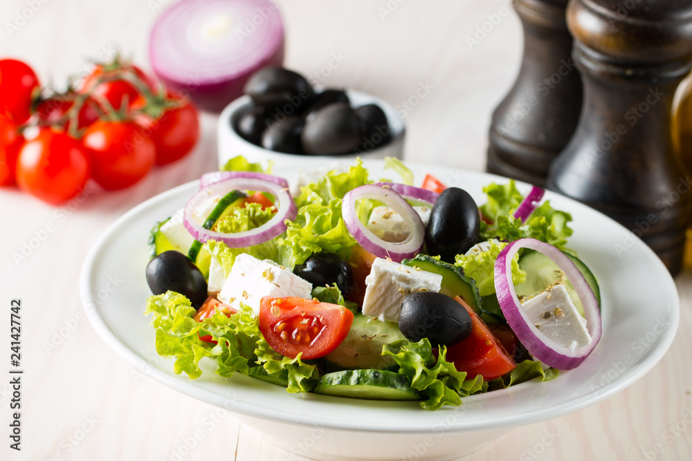 Fresh Greek salad with delicious ruccola, spinach, cabbage, arugula, feta cheese, red onion and cherry tomato on wooden background. Oil, salt and pepper. Healthy and diet food concept. Fresh Greek salad with delicious ruccola, spinach, cabbage, arugula, feta cheese, red onion and cherry tomato on wooden background. Oil, salt and pepper. Healthy and diet food concept.