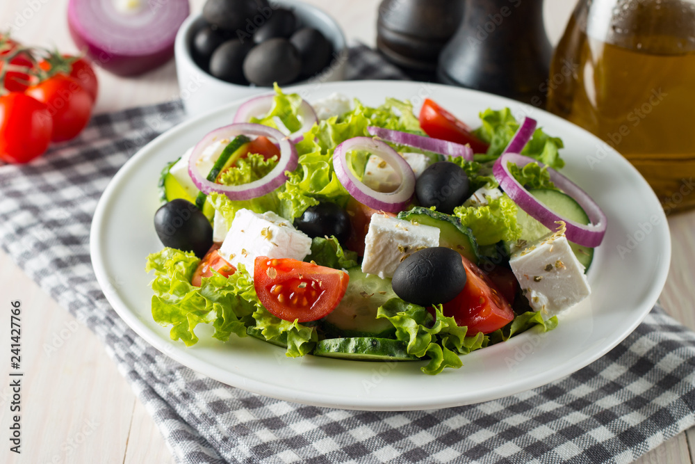Fresh Greek salad with delicious ruccola, spinach, cabbage, arugula, feta cheese, red onion and cherry tomato on wooden background. Oil, salt and pepper. Healthy and diet food concept. Fresh Greek salad with delicious ruccola, spinach, cabbage, arugula, feta cheese, red onion and cherry tomato on wooden background. Oil, salt and pepper. Healthy and diet food concept.