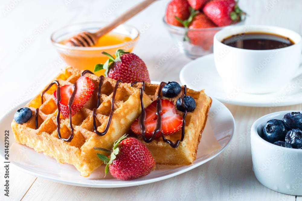 Fresh homemade food of berry Belgian waffles with honey, chocolate, strawberry, blueberry, maple syrup and cream. Healthy dessert breakfast concept with juice Fresh homemade food of berry Belgian waffles with honey, chocolate, strawberry, blueberry, maple syrup and cream. Healthy dessert breakfast concept with juice