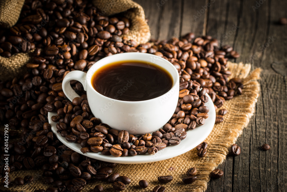 Fototapeta premium Coffee cup and beans on a rustic background. Coffee Espresso and a piece of cake with a curl. Cup of Coffee and coffee beans on table.