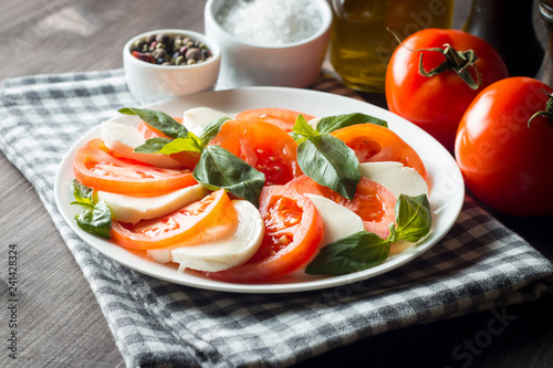 Photo of Caprese Salad with tomatoes  basil  mozzarella  olives and olive oil on wooden background. Italian traditional caprese salad ingredients. Mediterranean  organic and natural food concept.