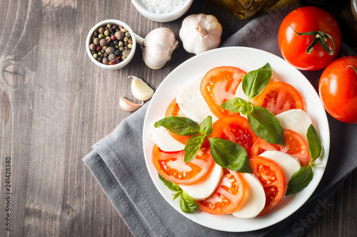 Photo of Caprese Salad with tomatoes, basil, mozzarella, olives and olive oil on wooden background. Italian traditional caprese salad ingredients. Mediterranean, organic and natural food concept.
