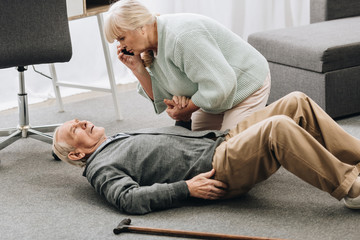 senior woman looking at husband who falled down with heart attack and dying