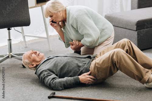 senior woman looking at husband who falled down with heart attack and dying