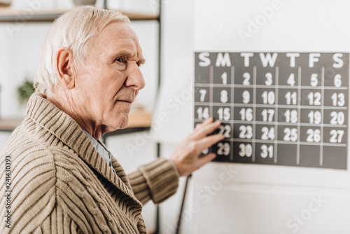 selective focus of senior man touching wall calendar and remembering dates