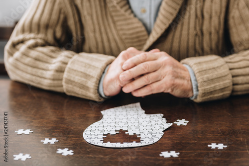 cropped view of senior man playing with puzzles on table photo