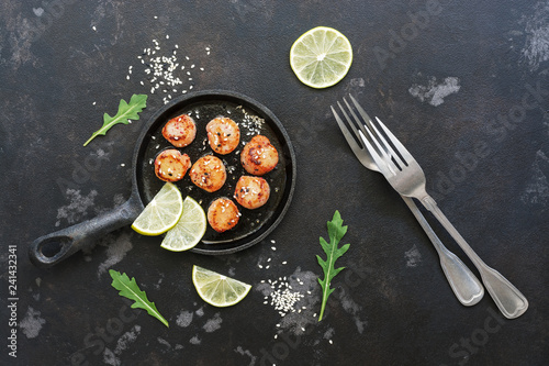 Scallops fried in a pan with lemon, on a black stone background. Top view, flat lay