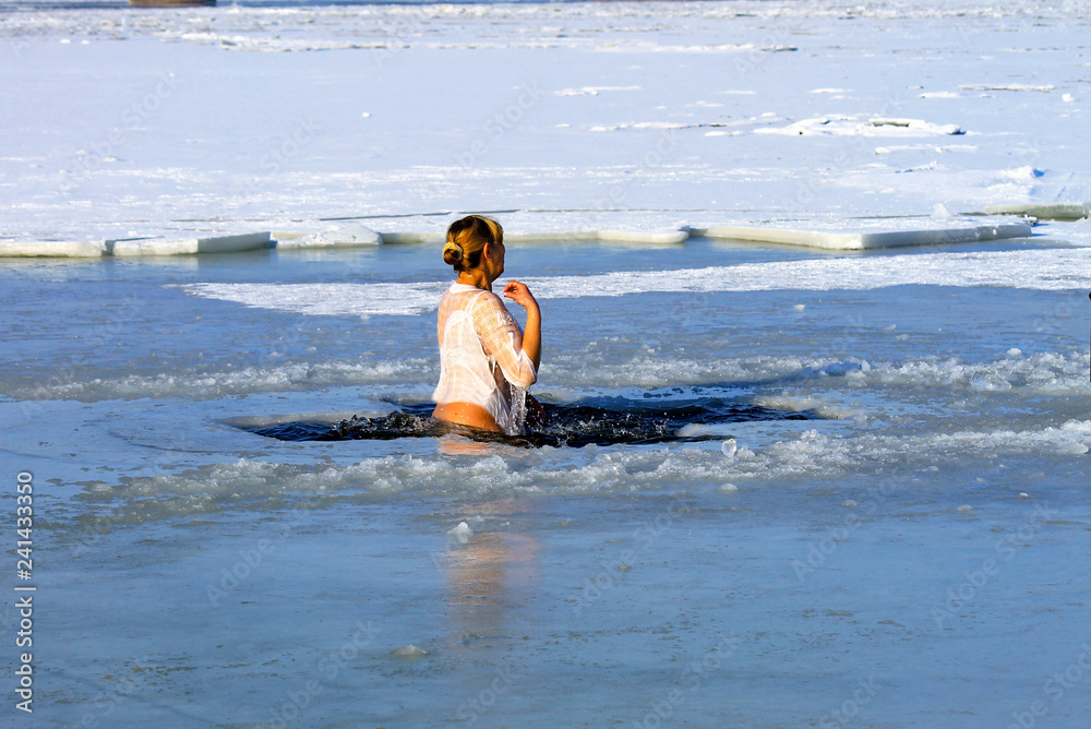 Winter sport. A woman swims in the winter river covered with ice during the holiday of Epiphany. Hardening