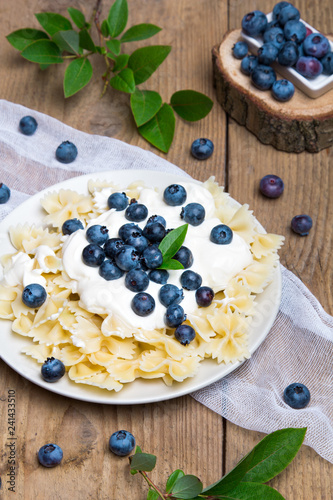Tasty pasta with fresh organic blueberries and vanilla cream. Sweet dinner on retro wooden table.