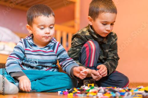 Two children playing with lots of colorful plastic blocks constructor sitting on a floor indoor. Two little brothers play constructor. Communication and friendship.