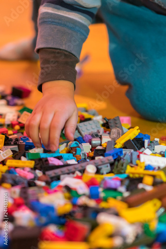 Close up of colorful plastic bricks on the floor. Early learning. Developing toys. Children s plastic constructor on the floor. Children s hands play a little constructor. vertical photo.