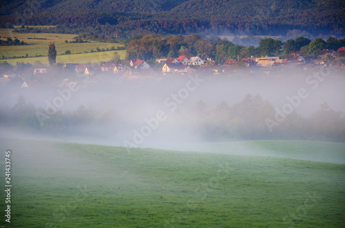 Morning landscape over village with meadows and trees covered by morning mist and beautiful sunrise light