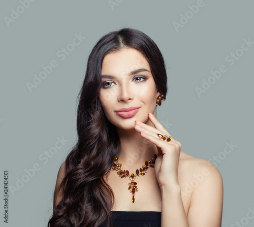 Smiling brunette woman with curly hair, makeup and amber ring, necklace, earrings