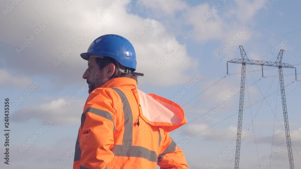 Electrician worker thinking trying to solve the problem, industrial electricity pylon in the background on cold winter day