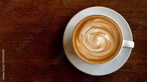 Hot coffee cappuccino latte spiral foam top view on wooden background