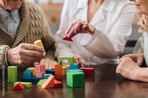 cropped view of retired couple and caregiver playing with wooden toys