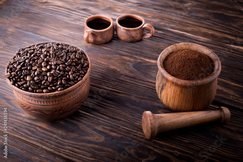 Two mugs of clay with coffee stand on a wooden board. Against the background of a mortar with ground coffee