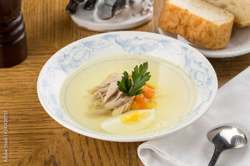 Low fat chicken broth with a half cooked egg and parsley in a glass bowl on wooden table